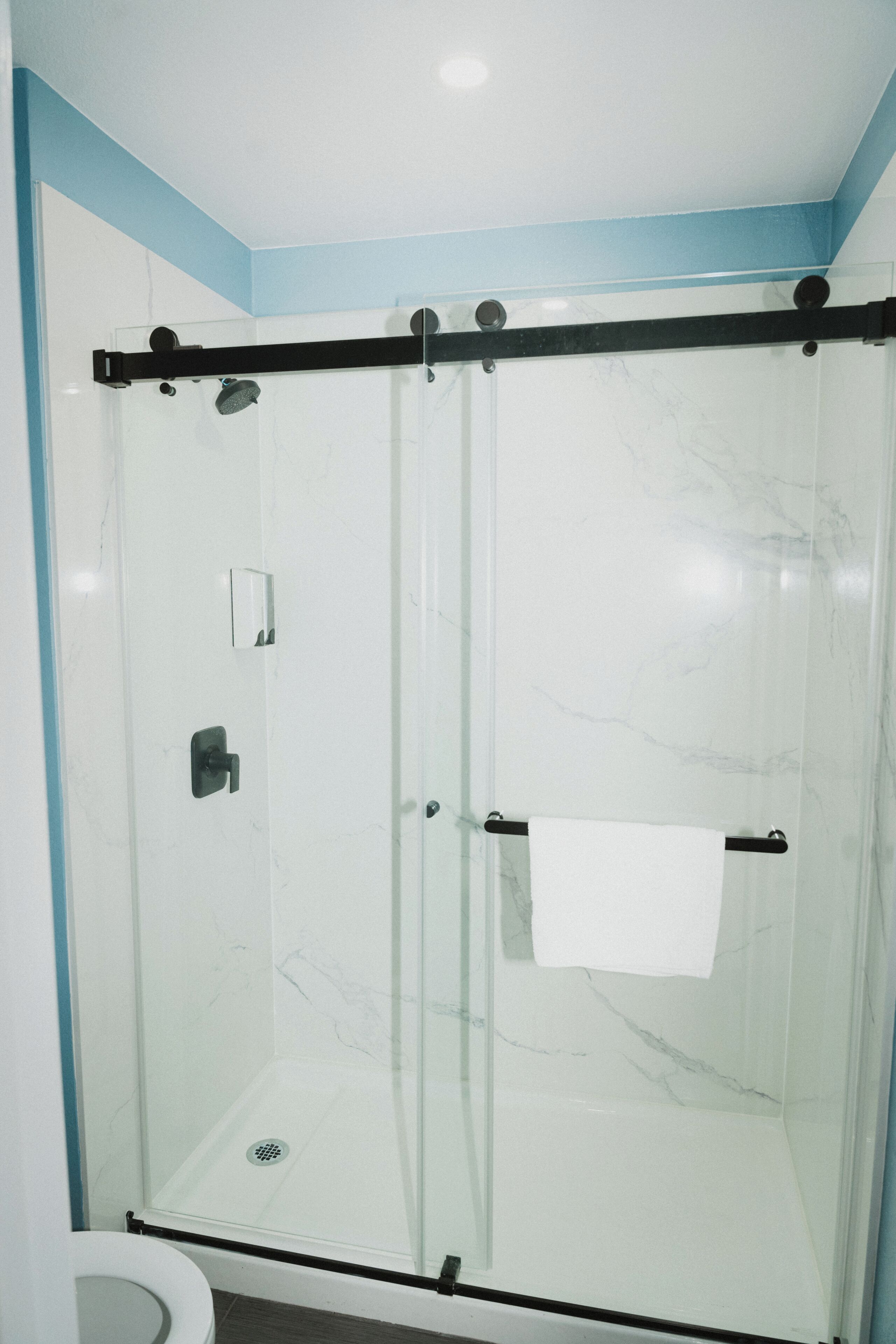 A glass-enclosed shower with a white marble wall, a towel rack, and a visible drain.