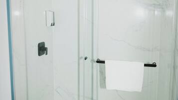 A glass-enclosed shower with a white marble wall, a towel rack, and a visible drain.