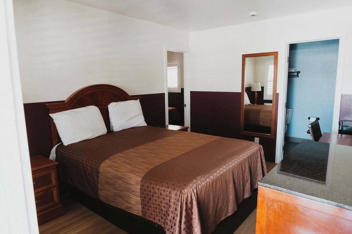 Una habitación de hotel con una cama grande, una mesita de noche de madera, un espejo y una pequeña mesa.