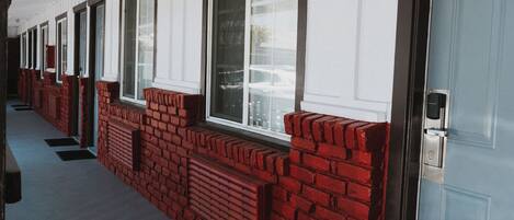 A row of hotel rooms with white walls and red brick accents, featuring large windows and a covered walkway.
