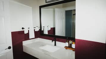 A bathroom with a white sink, black faucet, and a mirror above it. There are towels hanging on a rack and a bottle of shampoo on the counter.