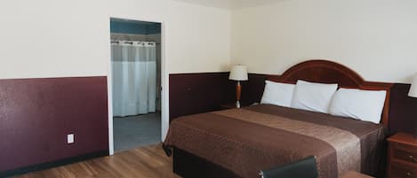 Una habitación de hotel con piso de madera, una cama con cubrecama marrón, una mesita de noche y una lámpara.