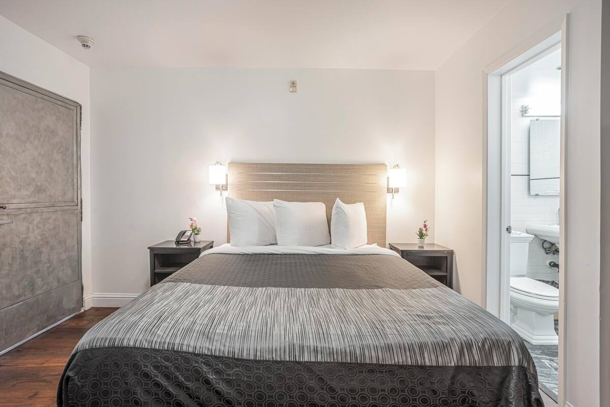 Una habitación de hotel moderna con una cama grande, dos mesitas de noche, una mesita auxiliar, un cabecero de madera y vistas al baño.
