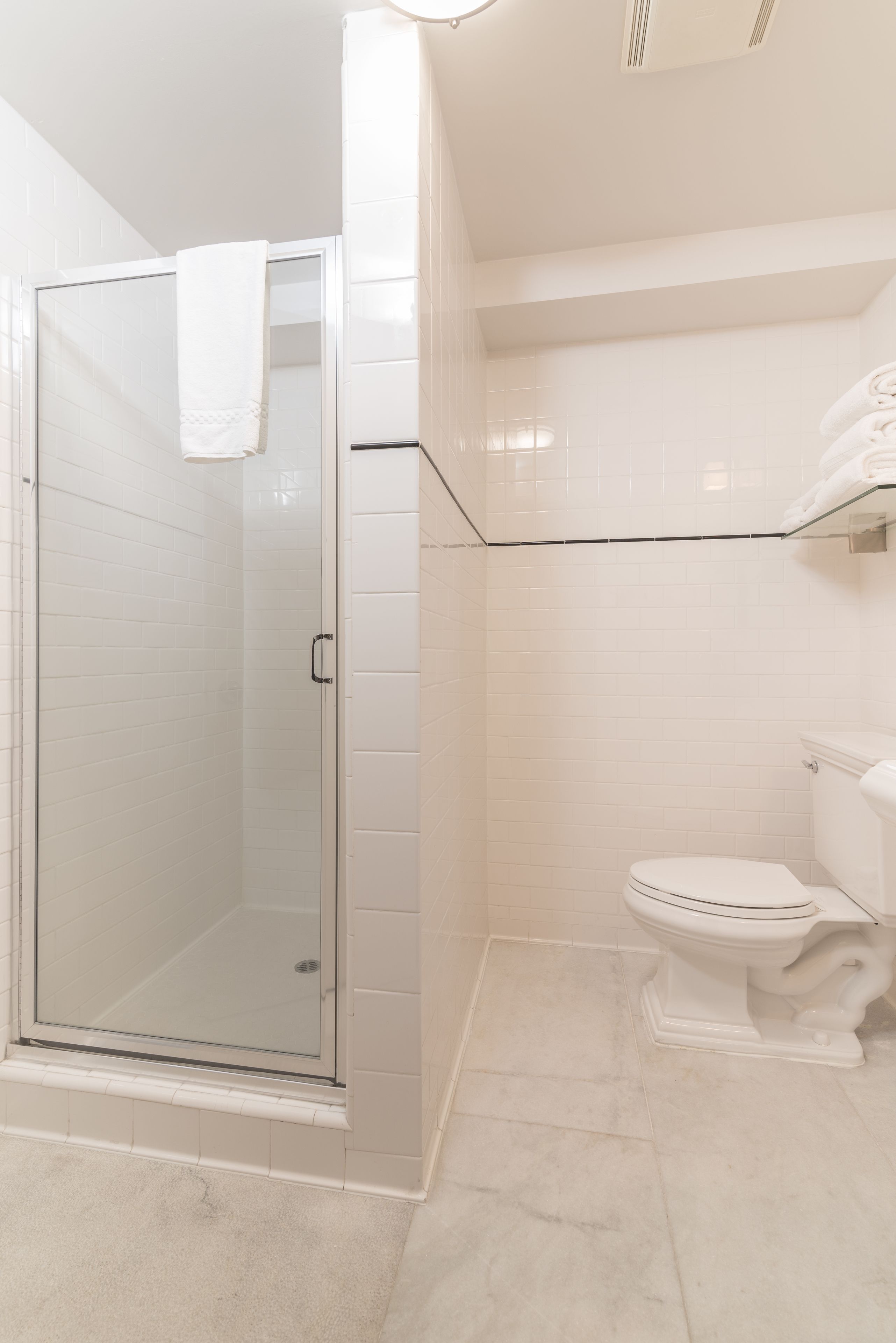 Ein Badezimmer mit Duschkabine aus Glas, Toilette und weiß gefliestem Boden.