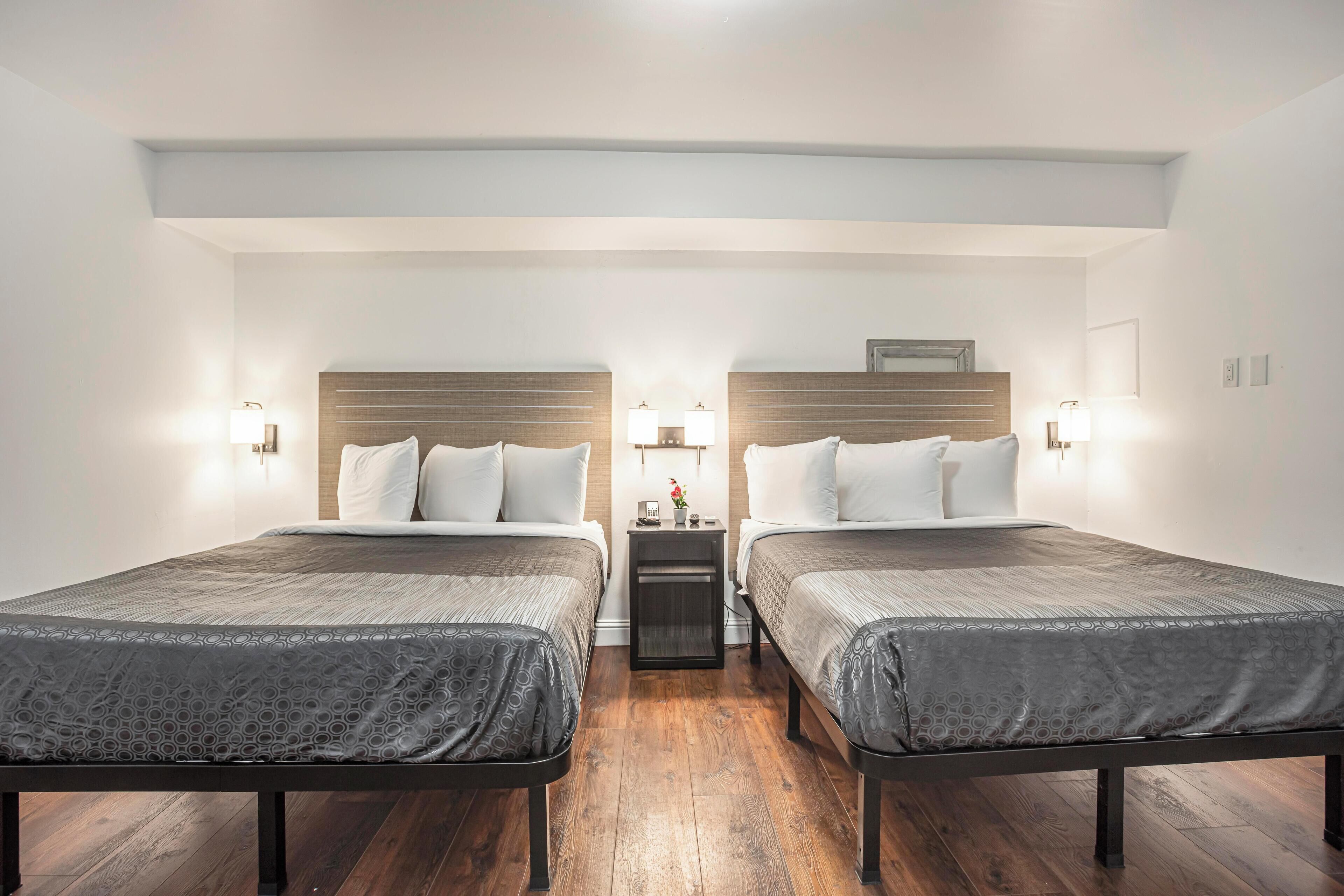 A double room with two beds, wooden headboards, bedside lamps, and a small table between the beds.