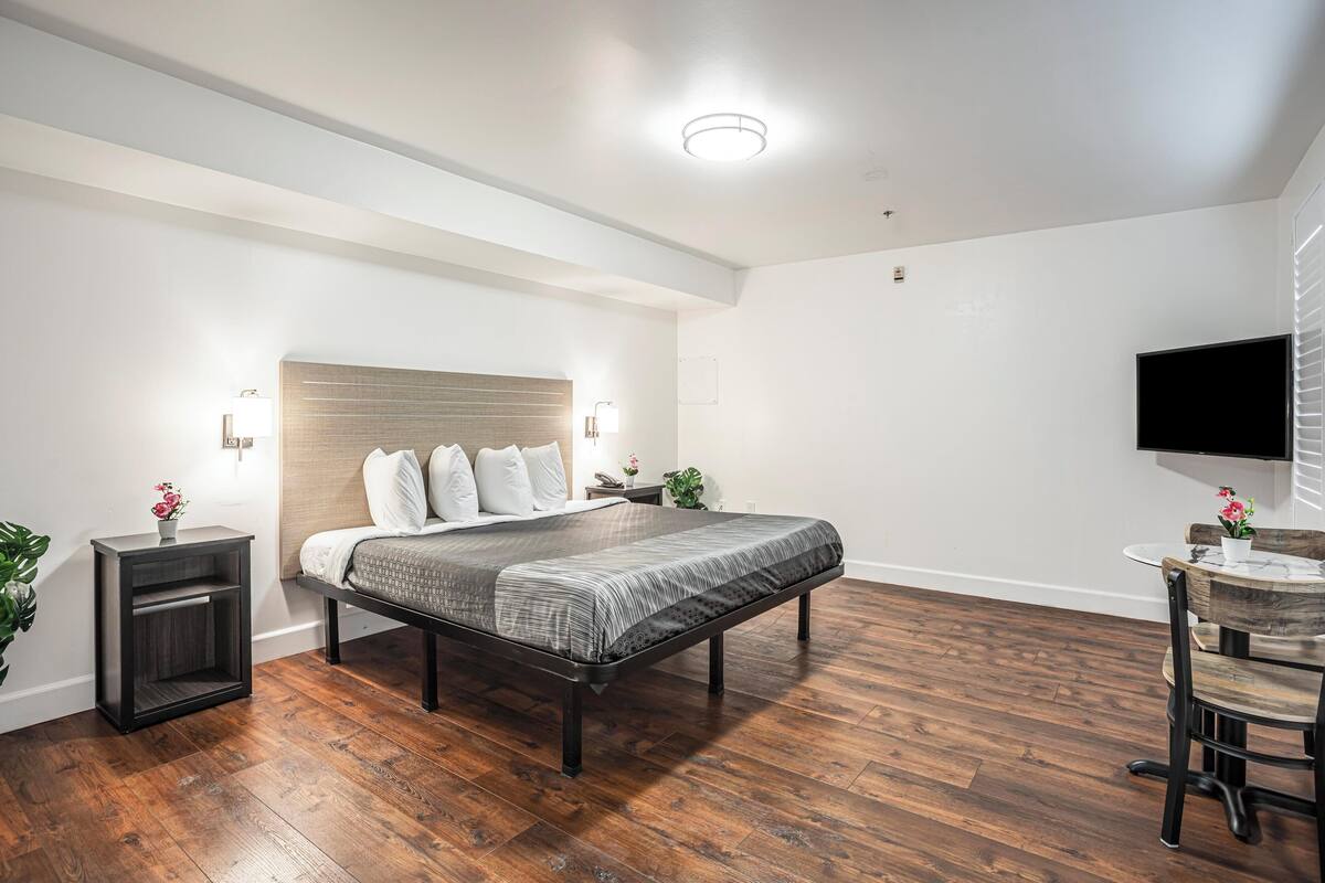 Un dormitorio moderno con una cama de madera, mesitas de noche, una pequeña mesa con sillas y un televisor montado en la pared.