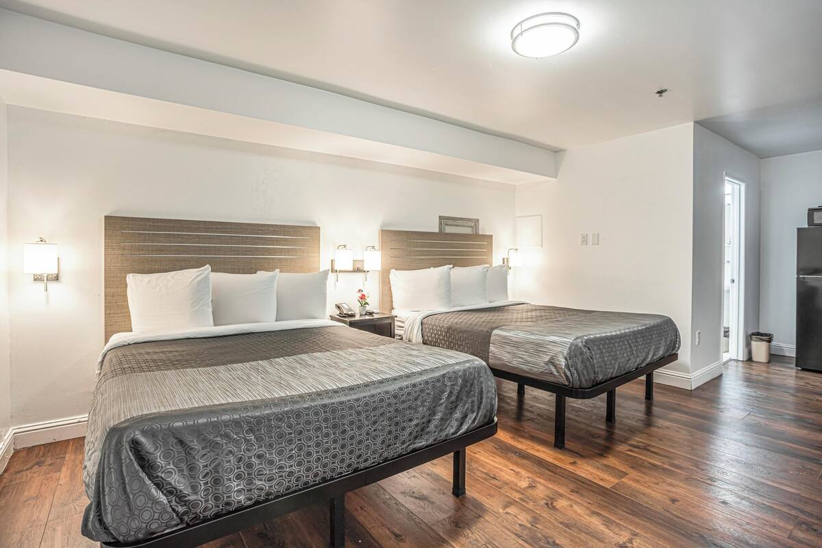 Habitación de hotel con dos camas, cabecero de madera, lámparas de noche y un refrigerador.