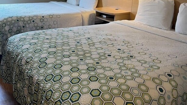 A hotel room with two beds, each with a patterned bedspread, a nightstand with a lamp, and a framed picture on the wall. - HomeTowne Studios & Suites by Red Roof Bentonville (Bentonville)