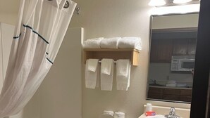 A bathroom with a bathtub, toilet, sink, and a mirror. - HomeTowne Studios & Suites by Red Roof Bentonville (Bentonville)