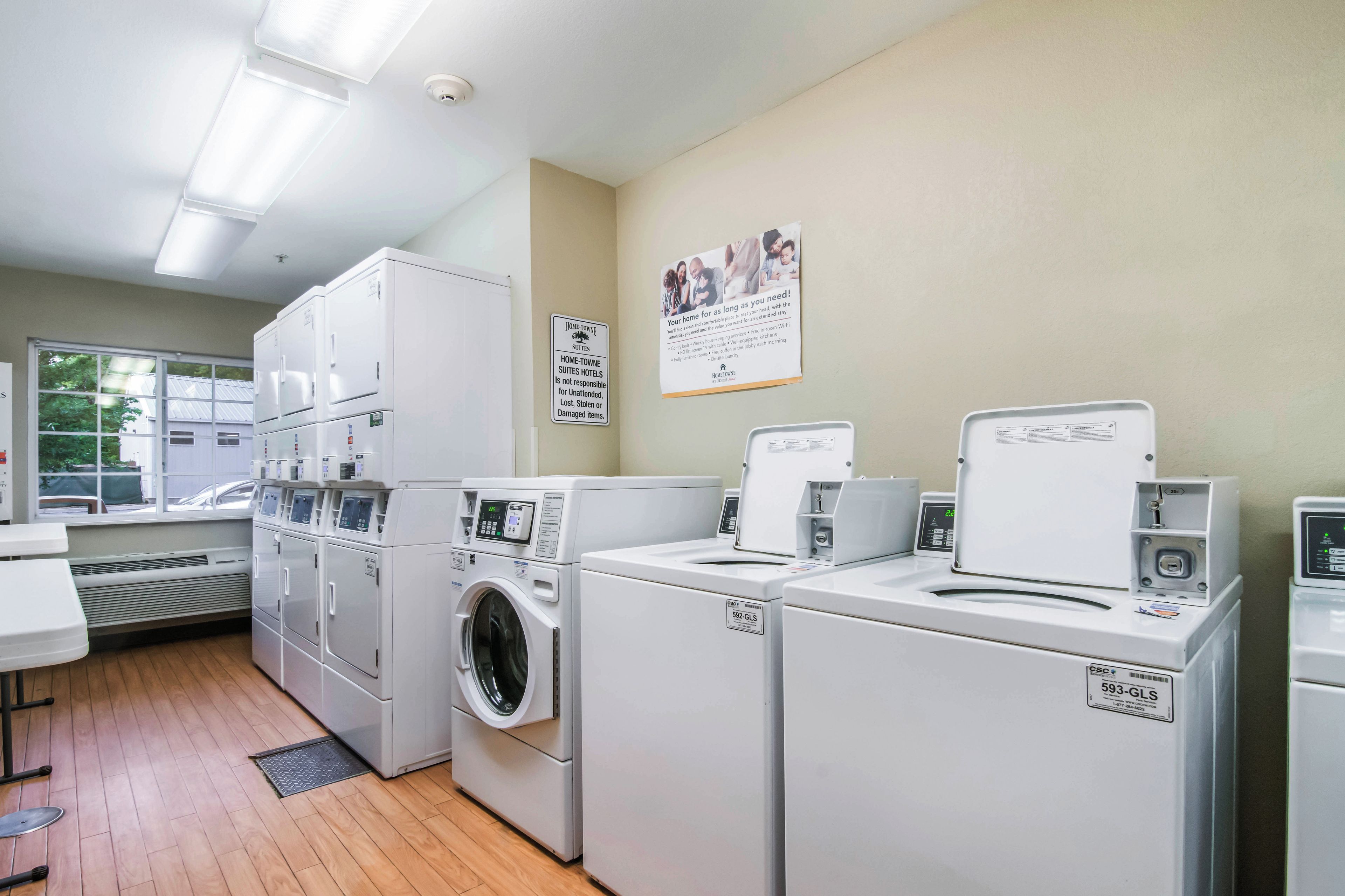 A laundry room with multiple washing machines and dryers, a vent system, and a sign indicating the hotel's laundry policy.