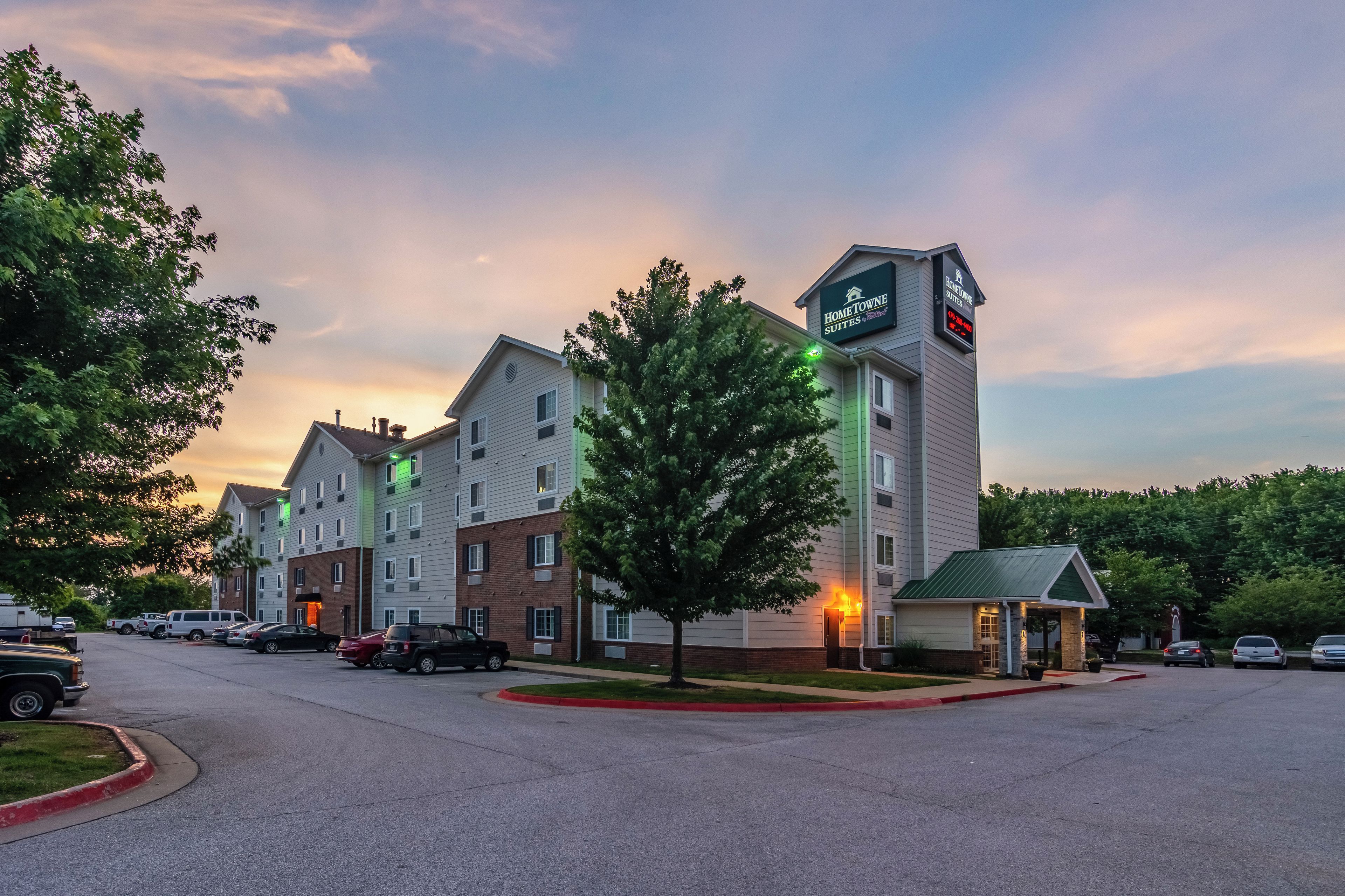 A hotel with multiple buildings, a parking lot, and a green-lit entrance.