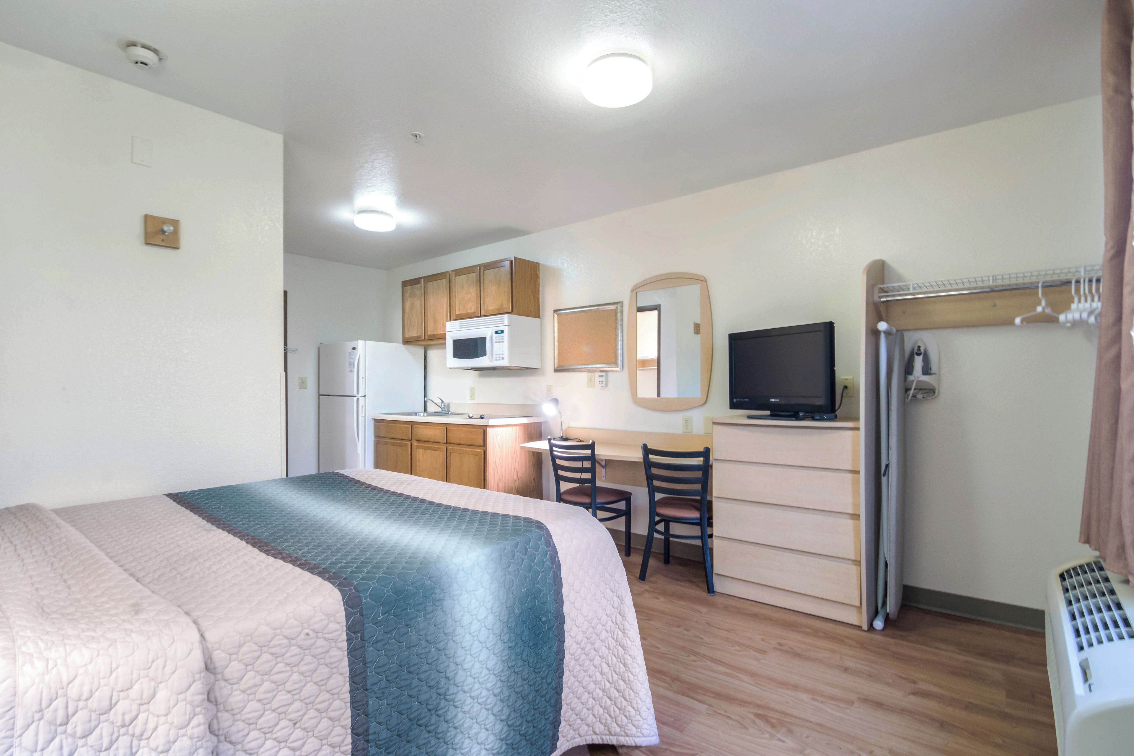 A compact room with a bed, a kitchenette, a television, and a desk.