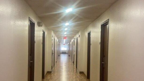 A long, narrow hotel corridor with wooden flooring and doors on both sides. - HomeTowne Studios & Suites by Red Roof Bentonville (Bentonville)