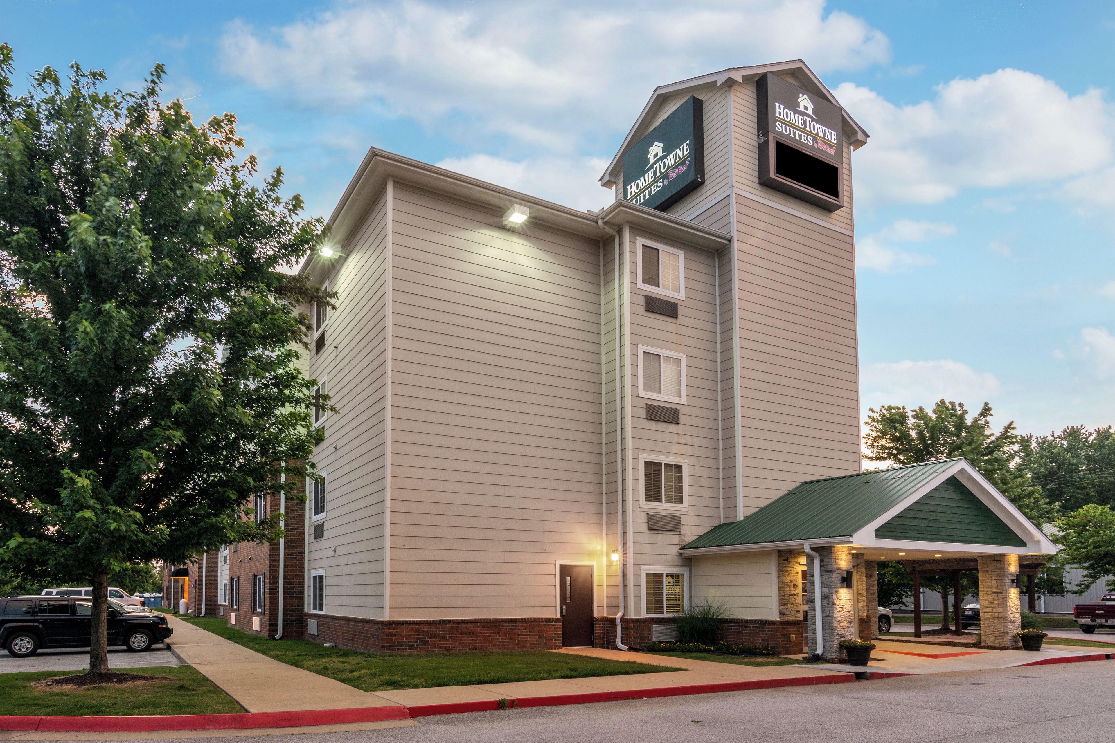 A hotel with a prominent sign, a covered entrance, and a parking area.