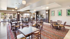 A spacious dining area with multiple tables and chairs, a patterned carpet, and a kitchen area in the background.