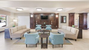 A spacious lobby with a beige sofa, blue armchairs, and a round table with a bowl centerpiece.