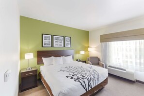 A hotel room with a large bed, two bedside tables, a chair, a window with curtains, and three framed pictures on the wall.
