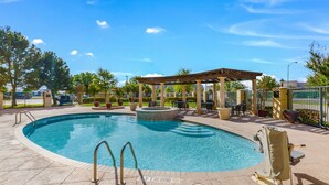 A swimming pool with a pergola, lounge chairs, and a hot tub.