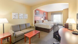 A hotel room with a sofa, two single beds, a desk, and a chair.