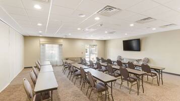 A conference room with long tables and chairs, a flat-screen TV on the wall, and a window with curtains.