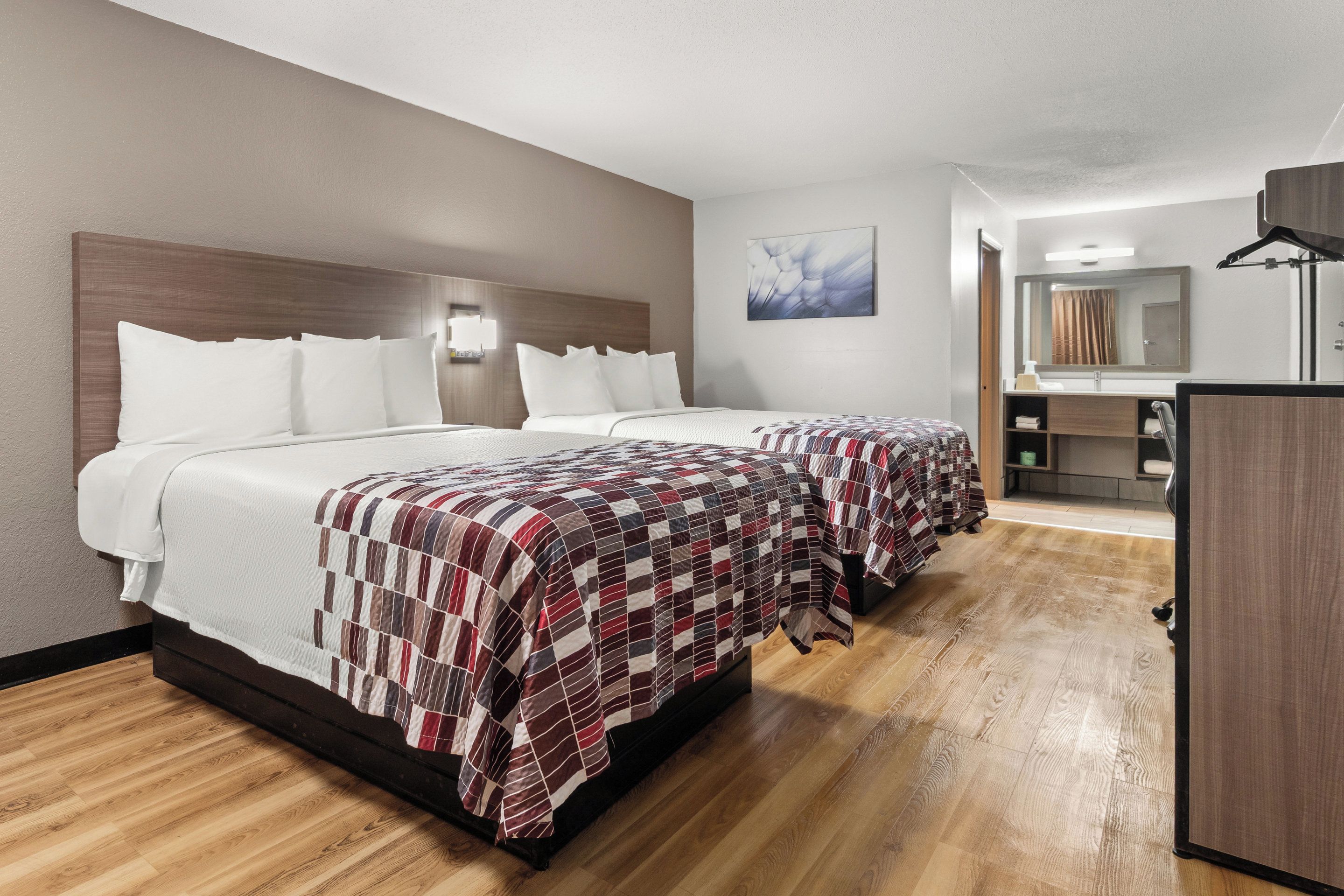 Habitación de hotel con dos camas, piso de madera, un espejo grande y un escritorio pequeño.