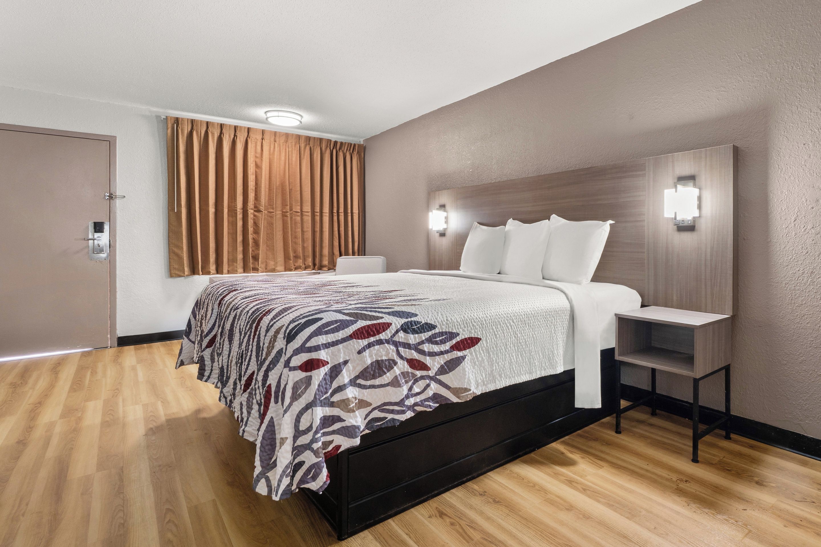Una habitación de hotel moderna con una cama grande, una mesita de noche, una lámpara de pared y una puerta con cerradura.