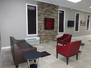 A Red Roof Inn lobby with a stone wall, two red chairs, a brown sofa, and a small table.