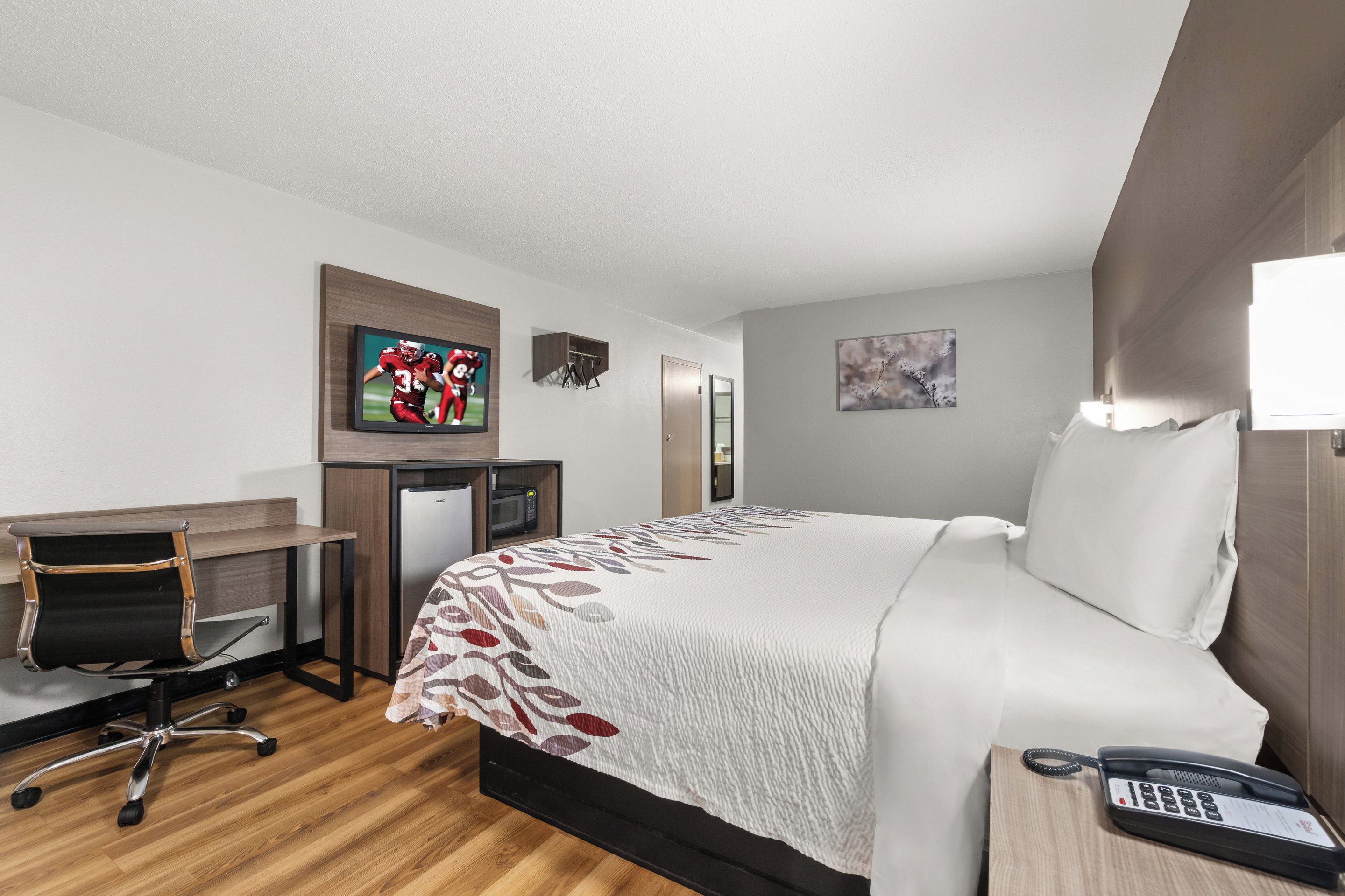 A hotel room with a bed, a desk with a chair, a television, a telephone, and a small cabinet.