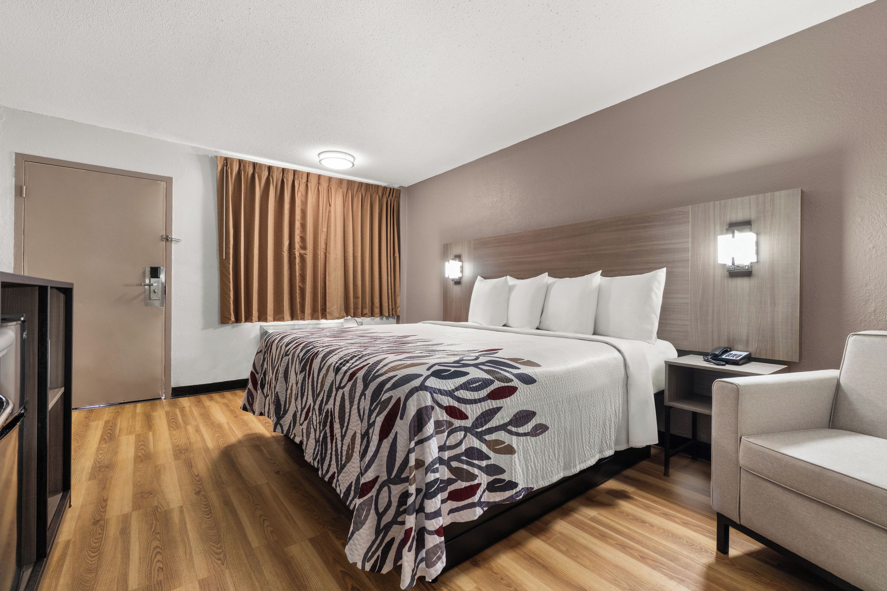 A hotel room with a bed, a desk, a chair, a wardrobe, and a door.