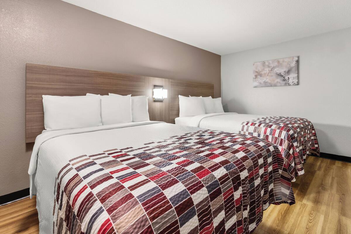 Ein Hotelzimmer mit zwei Betten, jedes mit unterschiedlicher Bettwäsche, einem Holz-Kopfteil, einer Wandleuchte und einem Bild an der Wand.