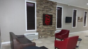 A Red Roof Inn lobby with a stone wall, two red chairs, a brown sofa, and a small table.