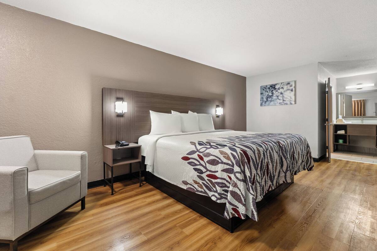 Ein Hotelzimmer mit einem Bett, einem Sessel, einem Nachttisch und einem Spiegel.