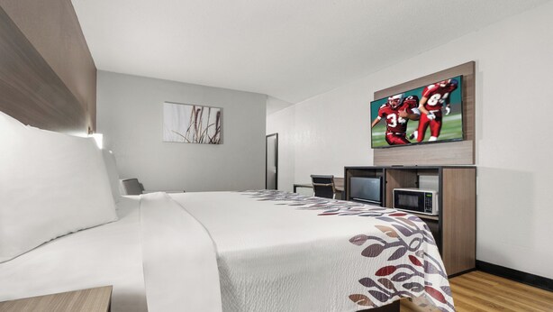 A modern hotel room with a large bed, a flat-screen TV, a microwave, and a small desk.