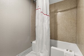 A bathroom with a white bathtub, beige speckled walls, and a white shower curtain with red trim.