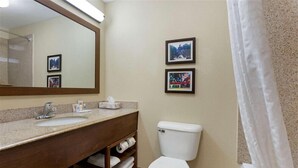 A bathroom with a sink, mirror, toilet, and two framed pictures on the wall. - Springplace Inn & Suites (Marion)