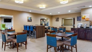 A hotel dining area with multiple tables and chairs, a kitchen area, and a television mounted on the wall. - Springplace Inn & Suites (Marion)