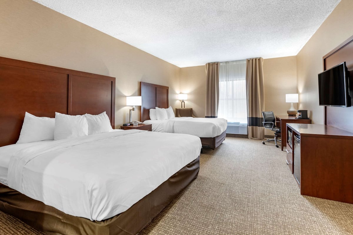 A hotel room with two beds, a desk, a chair, a TV, and a window with curtains.