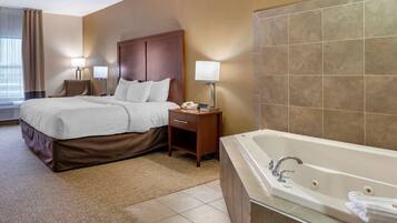 A hotel room with a large bed, a bedside table with a lamp, a telephone, and a bathroom with a bathtub and a glass shower enclosure.