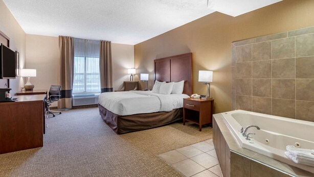 A hotel room with a bed, bedside tables, a desk with a lamp, a large bathtub, and a television on the wall. - Comfort Inn Louisville Southwest (Louisville)