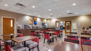A restaurant with multiple tables and chairs, a counter with food items, and a wall with a clock and a sign. - Comfort Inn Louisville Southwest (Louisville)