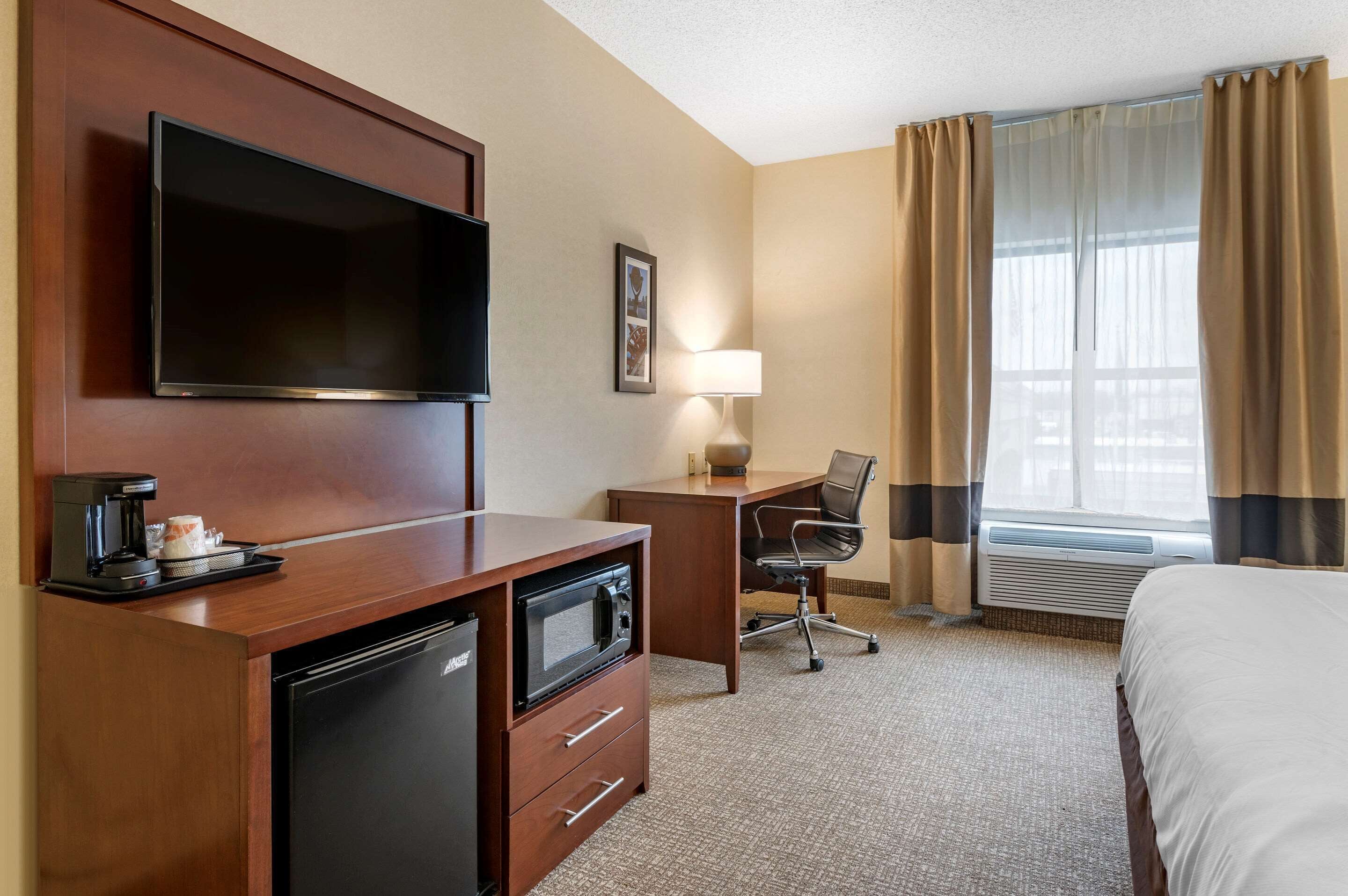 A hotel room with a flat-screen TV, a desk with a lamp, a microwave, a coffee maker, and a bed.