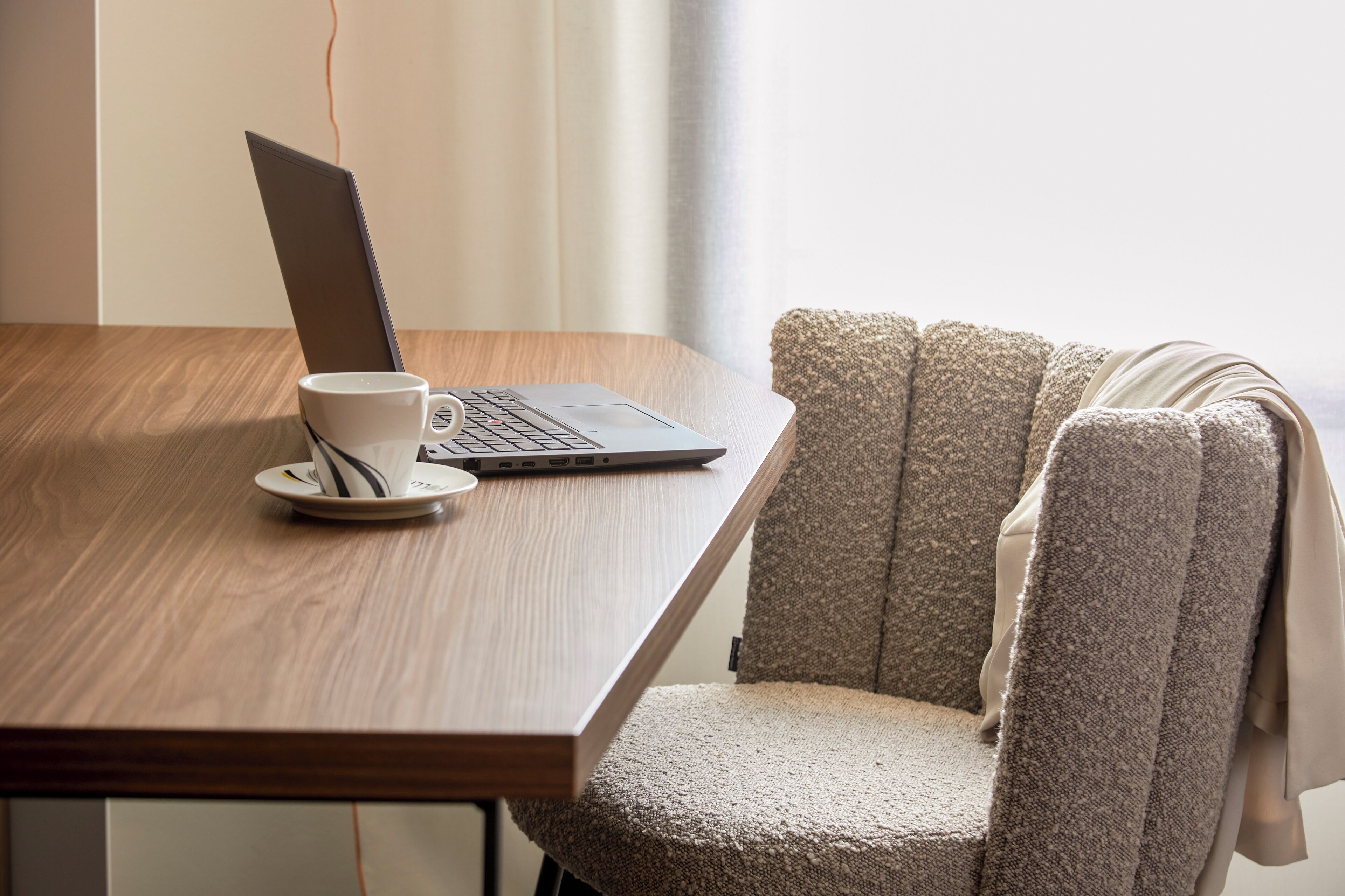 A laptop on a wooden table with a white cup and saucer beside it.
