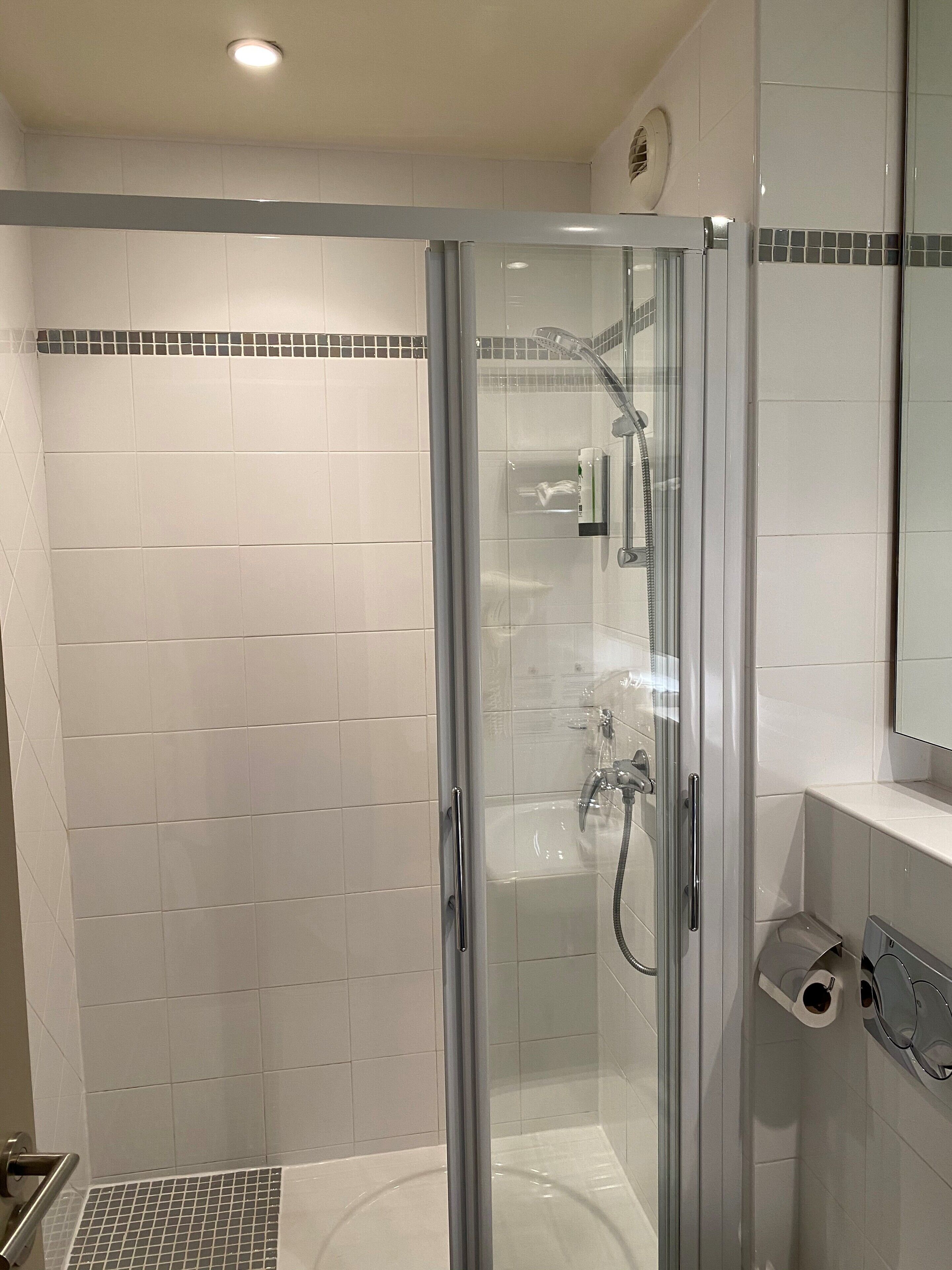 Een moderne badkamer met een douche met glazen wand, witte betegelde wanden, een wastafel en een spiegel.