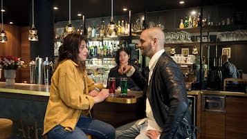 Un espace bar avec un comptoir, des luminaires suspendus et des étagères remplies de bouteilles et de verres.