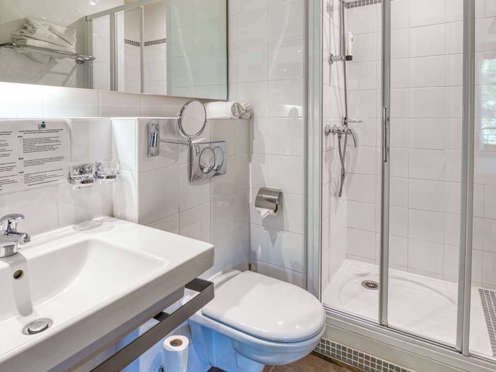 A modern bathroom with a white sink, a toilet, a glass shower enclosure, and a mirror.
