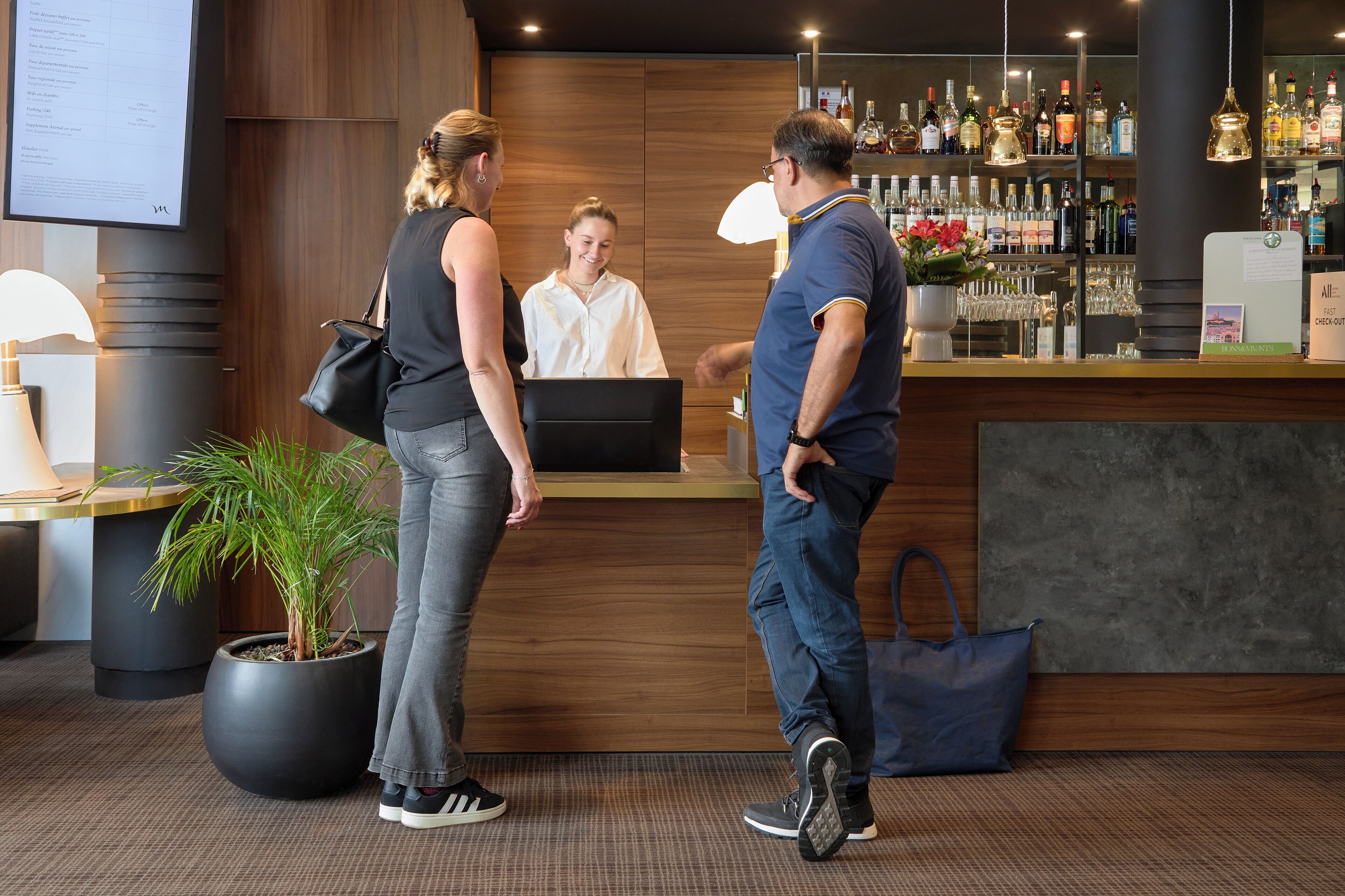 Un espace d’accueil avec un comptoir en bois, une plante en pot et un bar où sont exposées différentes bouteilles.