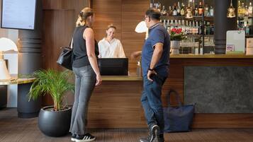 Un espace d’accueil avec un comptoir en bois, une plante en pot et un bar où sont exposées différentes bouteilles.
