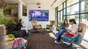 Un'area lounge moderna con sedute confortevoli, un grande schermo che mostra un gioco di corse e ampie finestre con vista sull'esterno.