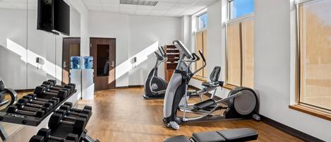 Ett gym med träningsutrustning, en tv och stora fönster.