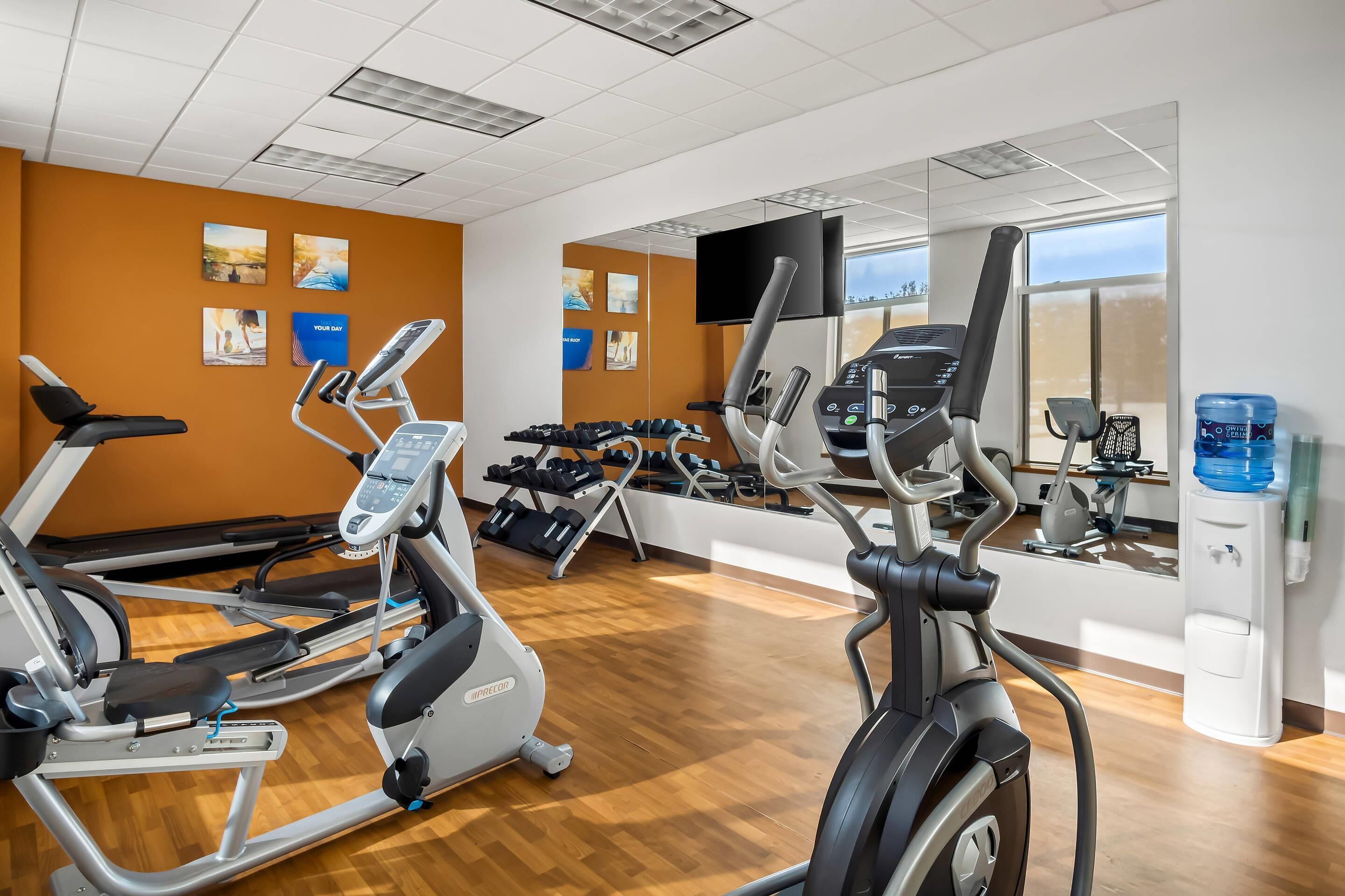 A gym with exercise equipment, a water dispenser, and a TV on the wall.